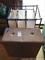 Front view of rolling hamper with three white fabric compartments and brown fabric storage bin in front