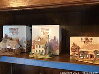 Three Lilliput Lane cottages displayed on shelf alongside their original boxes
