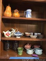 Full shelf shot showing various ceramic and pottery items including gourds, bowls, pitchers, teapot, and vases