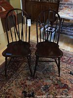 Pair of dark wood Windsor chairs with curved spindle backs placed on a patterned rug indoors.