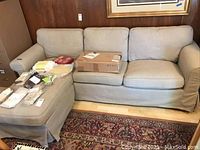 Light beige IKEA Ektorp three-seat couch with matching ottoman, showing fabric, cushions, and additional set of covers in a sealed box on the couch seat.