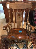 Front view of wooden rocking chair showing curved backrest with carved wood details and turned arm supports.