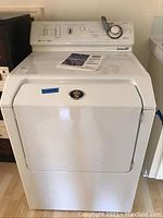 Full front view of white dryer with manual on top