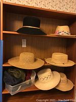 Full view of the shelf with assortment of seven hats displayed and a plastic bin with baseball caps underneath.