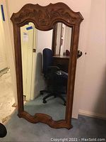 Full view of the wood framed mirror standing upright against a wall showing its overall size and shape