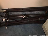 Photo of disassembled dark brown metal bed frames showing side rails and caster wheels on carpet.