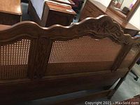 Straight-on view of full headboard showing carved top rail and woven cane panels