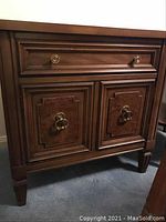 Front view of the wooden nightstand showing drawer and double-door cabinet with ring pull handles and decorative paneling.