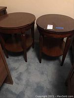 Pair of oval end tables standing side by side on carpeted floor showing tops and sides