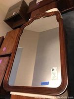 Full view of the wall mirror showing rectangular shape, wooden frame, slight curve at corners, and ornate carved details at top center.