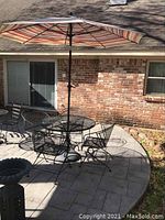 Full view of round wrought iron mesh table, four chairs, umbrella and stand on patio