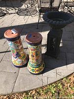 Two colorful ceramic planters with hand-painted Talavera style patterns and a black metal stand on a stone patio.