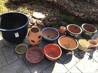 Photo showing full lot of ceramic and terracotta planters and pots arranged on the ground with river stones and grass nearby.