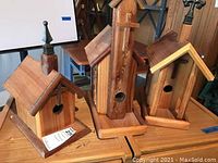 Three wooden handmade birdhouses displayed on a wooden table, showing their size and finish.