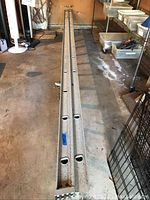 Photo showing full length of the aluminum extension ladder laid flat on the ground in a storage area with visible wear and weathering.