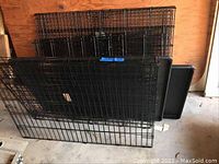 Multiple black metal wire crate panels leaning against a wall with two black plastic trays behind them.