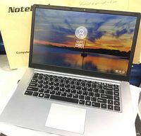 Front view of notebook laptop powered on in open box, showing screen and keyboard