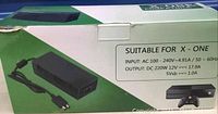 Green and white box of Xbox One AC adapter showing input and output electrical specifications