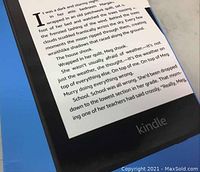 Close-up of Kindle e-reader screen displaying black and white text from a book, powered on, with visible Kindle branding at the bottom.