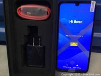 Smartphone powered on displaying setup screen alongside charger and USB cable in foam packaging