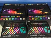 Four unopened Romwish Smart LED strip light boxes arranged in two rows on a flat surface showing front packaging with colorful LED images and logos.