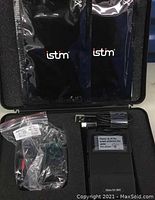 Overall view of the iStim muscle stimulator device and accessories in the open case showing device, leads in plastic bag, USB cable and electrode pads.