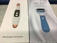 Side-by-side boxes of the blackhead instrument and Abody rechargeable callus remover showing product images and branding on the front.
