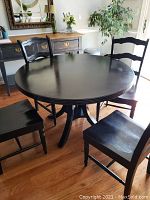 Full view of the round black dining table with four matching chairs around it in a room with wooden flooring and other furniture.