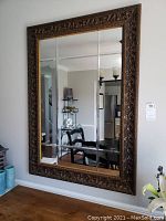 Full front view of the large wall mirror hanging on a wall, showing the ornate carved frame and the segmented reflective glass surface.