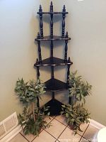Full view of the black five-tier corner shelf with two faux plants on each side