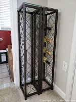 Pair of metal wine bottle racks with glass tops, arranged side-by-side in a corner with some bottles inside each rack.