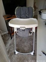 Full view of highchair showing seat, tray, and metal frame with wheels.