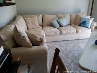 Photo showing the full sectional sofa with beige upholstery and four throw pillows, corner configuration.