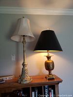Photo of two lamps on a wooden sideboard; the brass pineapple lamp with black shade is shown on the right side.