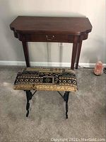 Front view of wood wall table with drop leaf and upholstered bench beneath it showing fabric pattern and table drawer handle.