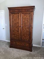 Front view of large wooden Ethan Allen entertainment media center with two closed doors and bottom drawer, showing detailed wood grain and finish.