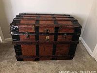 Front view of vintage wooden trunk with black metal reinforcements and lock.
