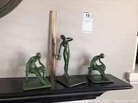 Three green patina cast metal sculptures on display with ruler for scale