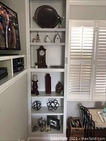 Photo of white built-in shelves showing various decorative items including vintage wooden clock, birdhouse, figurines, candle holder, vase, black spheres, and framed photo.
