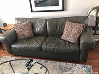 Full frontal view of olive green leather sofa with two decorative pillows, showing overall condition and style.
