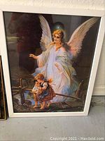 Framed print artwork showing an angel in white robes guiding two children over a wooden bridge, contained in a white frame.