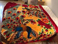 Blanket spread out showing full peacock and floral design with red border.