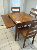 Full view of the wooden table with one leaf extended and four matching wooden chairs around it.