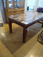 Wide shot showing full marble top and wooden legs of the dining table in a room with wooden floors and cabinet behind.