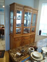Front view of the wood china cabinet showing the glass doors on the top portion, with three main glass doors and visible shelves inside. Lower portion has drawers and cabinet doors.