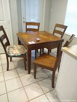 Four solid wood dining chairs arranged around a wooden dining table. Two chairs have floral cushions on the seats.