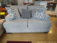 Front view of beige loveseat with three decorative pillows and nailhead trim