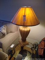 Full view of heavy ceramic or plaster table lamp with beige shade on glass table beside couch.