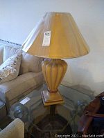 Full view of the lamp showing the ornate base and fabric lampshade on a glass table near sofa.
