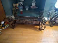 Front view of glass top end table showing scalloped glass surface, wrought iron legs, and marble inset on wooden bottom shelf.